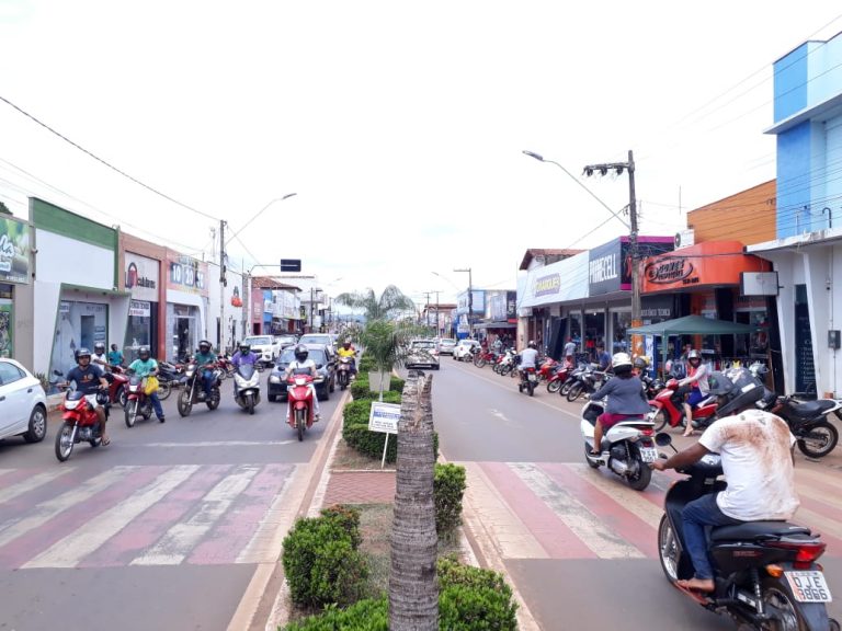Avenida com duas mãos é vista de frente há motos e carros estacionados.