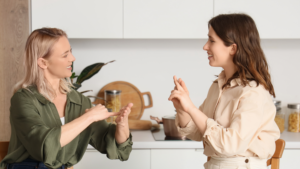 Duas mulheres, uma de frente para outra, fazem o uso de sinais.